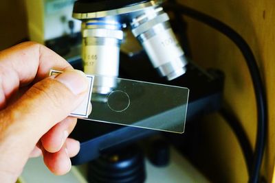 Cropped hand holding glass slide by microscope