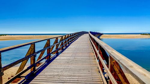 Wooden footbridge over sea against clear blue sky