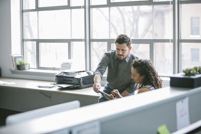 Colleagues using tablet computer while sitting at desk in office