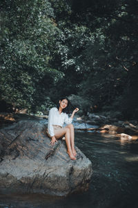 Portrait of young woman sitting on rock in forest