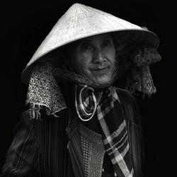 Portrait of mature woman wearing hat standing against black background