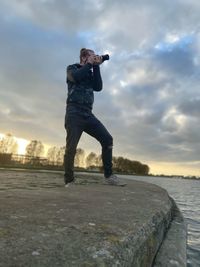 Low angle view of man photographing while standing against sky during sunset
