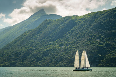 Sailboat sailing on sea by mountains against sky