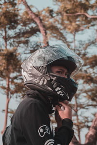 Side view of man wearing helmet against trees