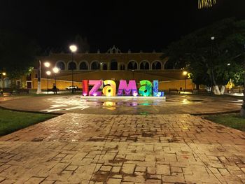 Illuminated street lights on footpath by building at night