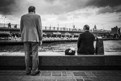 Rear view of men sitting on bridge in city against sky