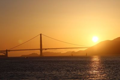 Suspension bridge over sea against sky during sunset