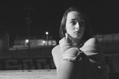 Thoughtful woman sitting on footpath at night