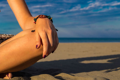Woman sitting on the beach with closeup of arm with bracelet and nail polish and knee with shadow