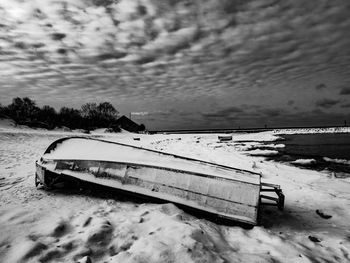 Abandoned boat on snow covered shore against sky