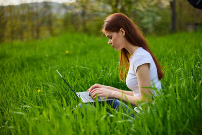 Young woman using laptop on field