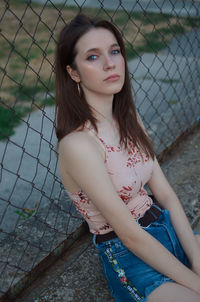 Portrait of young woman standing against chainlink fence