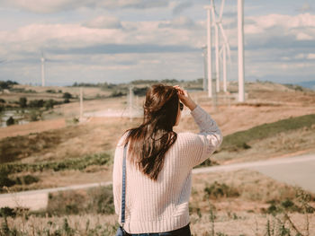 Rear view of woman standing against windmills on landscape