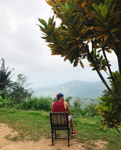 Rear view of man sitting on landscape against sky