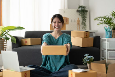 Smiling woman holding box sitting at home