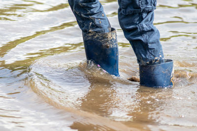Young boy wading through high tide with blue gumboots after a flood has broken the protecting dike