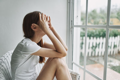 Side view of depressed woman sitting by window