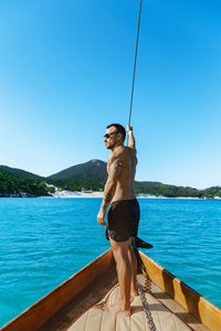 Shirtless young man standing on boat at sea