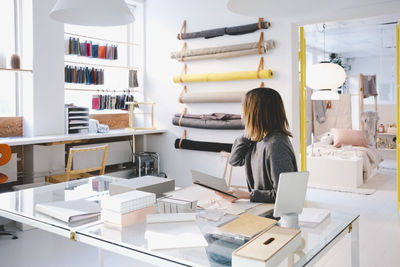 Female entrepreneur looking at fabric swatches while holding note pad at table in store