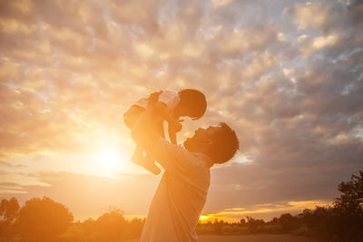 Low angle view of father and son against sky during sunset