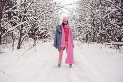 Woman enjoy in pink clothes a jacket a knitted scarf and a hat stands in a snowy forest in winter