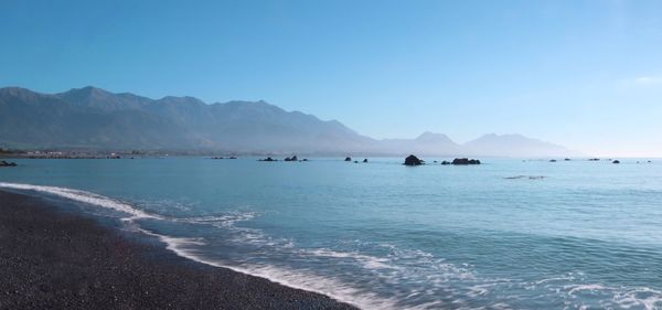 Scenic view of sea and mountains against clear blue sky