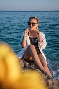 Young woman sitting on sunglasses against sea