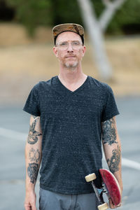 Portrait of adult male standing holding skateboard looking at camera