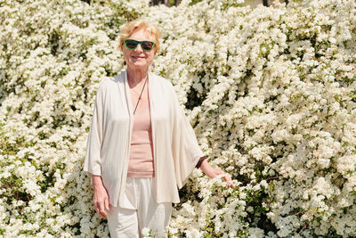 Elderly woman posing among bushes with white flowers