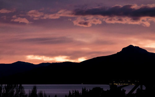 Silhouette mountains by lake against sky during sunset