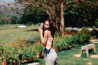 Young woman photographing with mobile phone while standing on plants