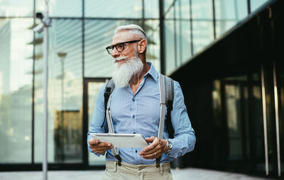 Senior hipster holding digital tablet against building