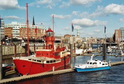 Fishing boats moored at harbor in city against sky