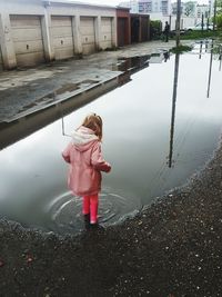 Rear view of girl standing in puddle on street during rainy season