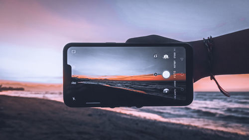 Close-up of smart phone against sunset sky