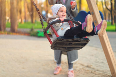 Cheerful cute girl sitting on swing at playground