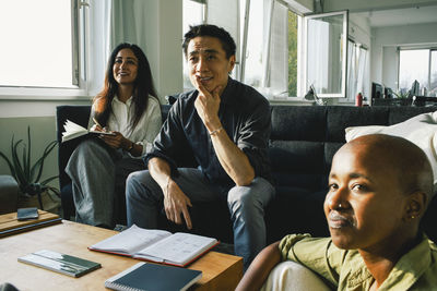 Businessman with hand on chin sitting with female colleagues during meeting at office