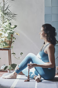 Side view of woman meditating while sitting by potted plants at home