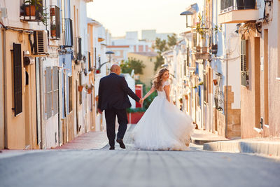 Rear view of friends walking on street amidst buildings