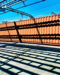 Shadow of fence on building against blue sky