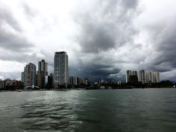 City at waterfront against cloudy sky