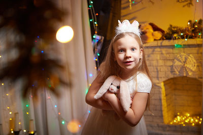 Portrait of young woman standing against illuminated christmas tree at night