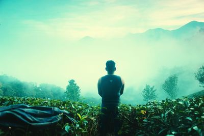 Rear view of man standing on field against sky