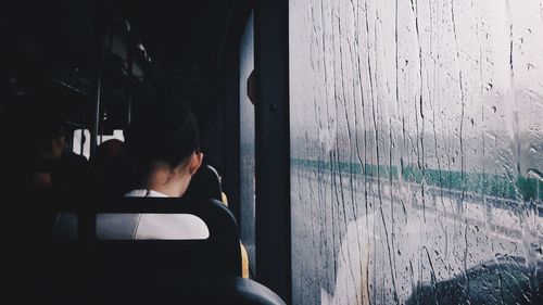 Rear view of woman relaxing by wet window in bus during rainy season