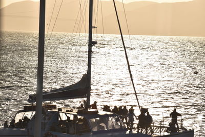 Silhouette people in sea against sky during sunset
