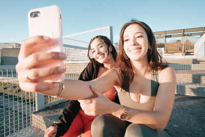 Smiling females friends taking selfie sitting outdoors