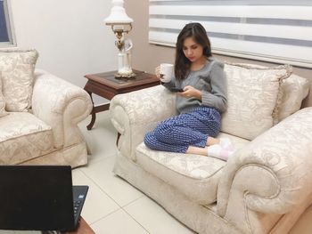 Full length of woman using mobile phone while sitting on bed