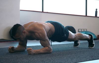 Full length of shirtless man doing push-ups on floor in gym