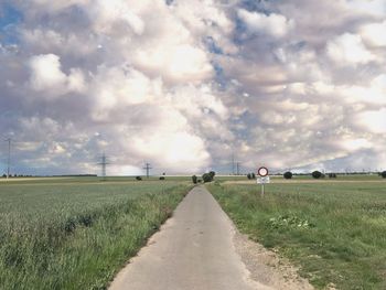 Empty road amidst field against sky