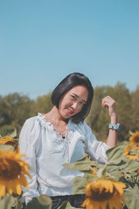 Young woman standing by flowering plants against sky